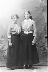 Studioportrett av to unge kvinner i helfigur.