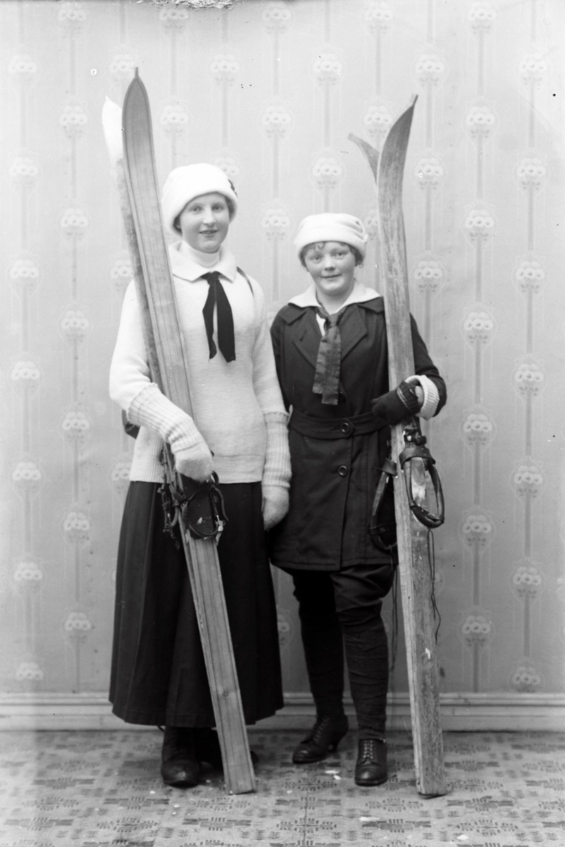 Studioportrett av to kvinner med varme klær og ski.