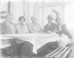 En mann og fire kvinner ved bord utenfor Lyng Olsens hus i P