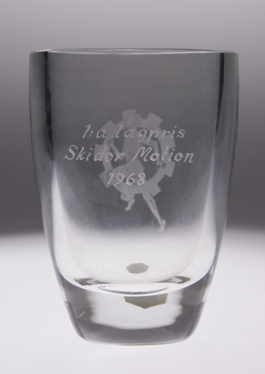 Pokalen har inskriptionen 1:a lagpris Skidor Motion 1968 Pokalen har oval form och kommer från Kosta Glasbruk Pokalen har ingraverat bilden av en löpare.