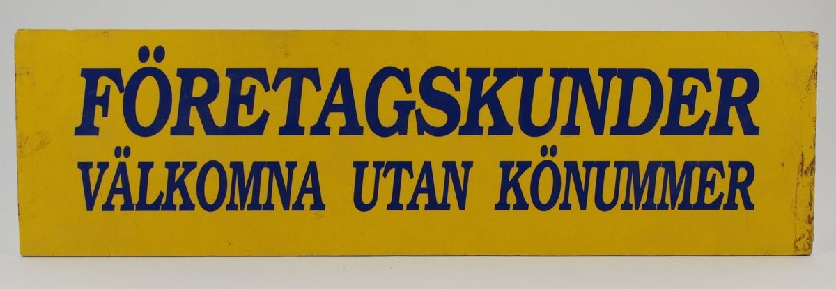 Postkassaskylt i plast, gul med text i blått i kursiva versaler: FÖRETAGSKUNDER VÄLKOMNA UTAN KÖNUMMER.