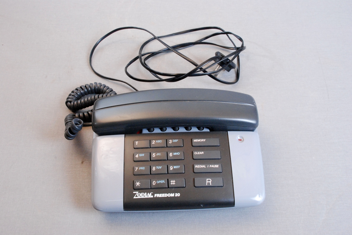 Telefonapparat med tastatur, telefonrør med ledning og kabel for veggkontakt. Apparatet hadde innlagt kode for svar ved varsel om storbrann.