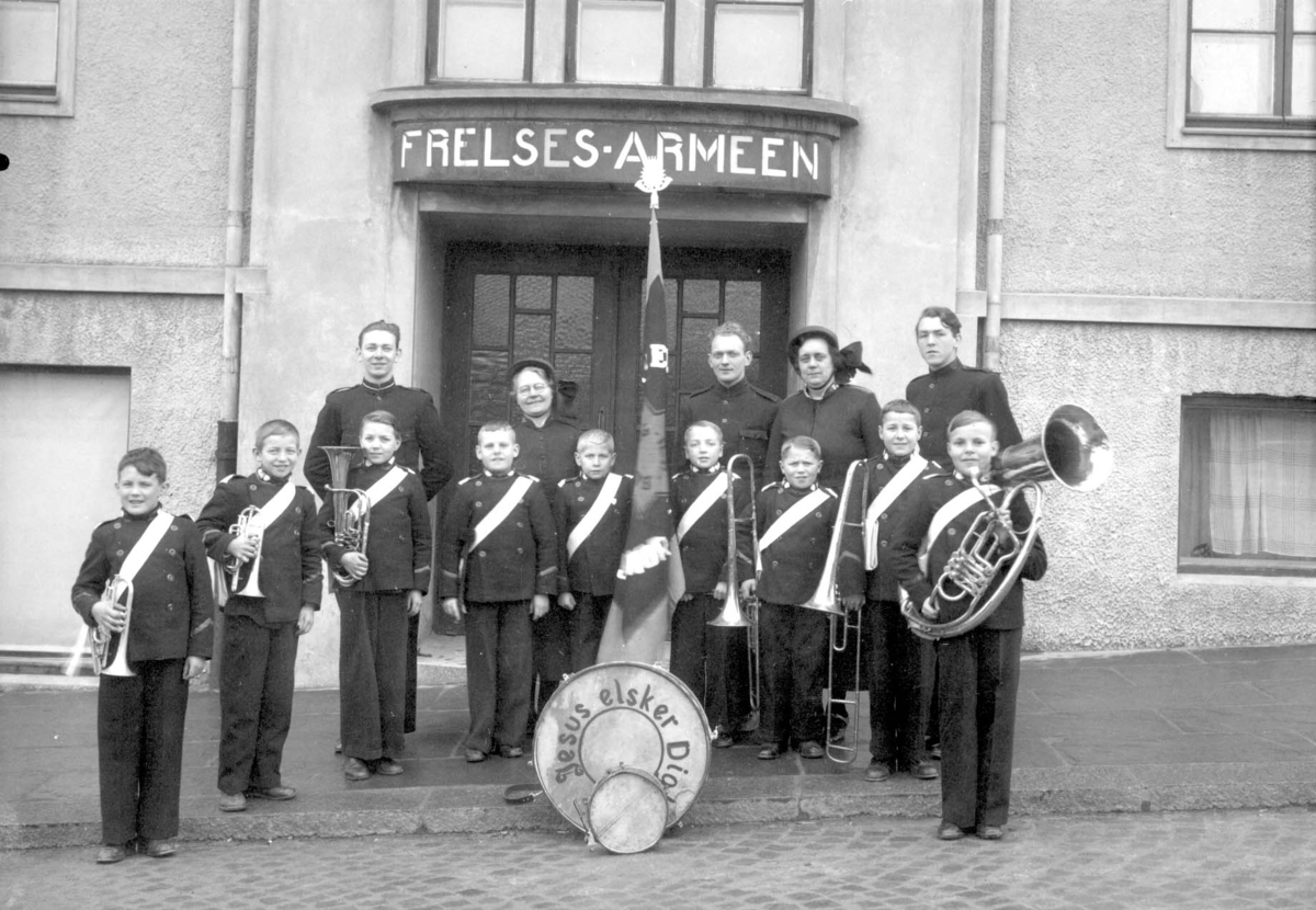 Frelsesarmeens musikkorps foran armeens hus i Skjoldavegen. Ni gutter i 10 - 13 års alderen med fem voksne bak. Instrumenteringen består av 2 kornetter, 1 alt, 2 tromboner og bass(tuba) samt dus(tromme) og skarptromme.