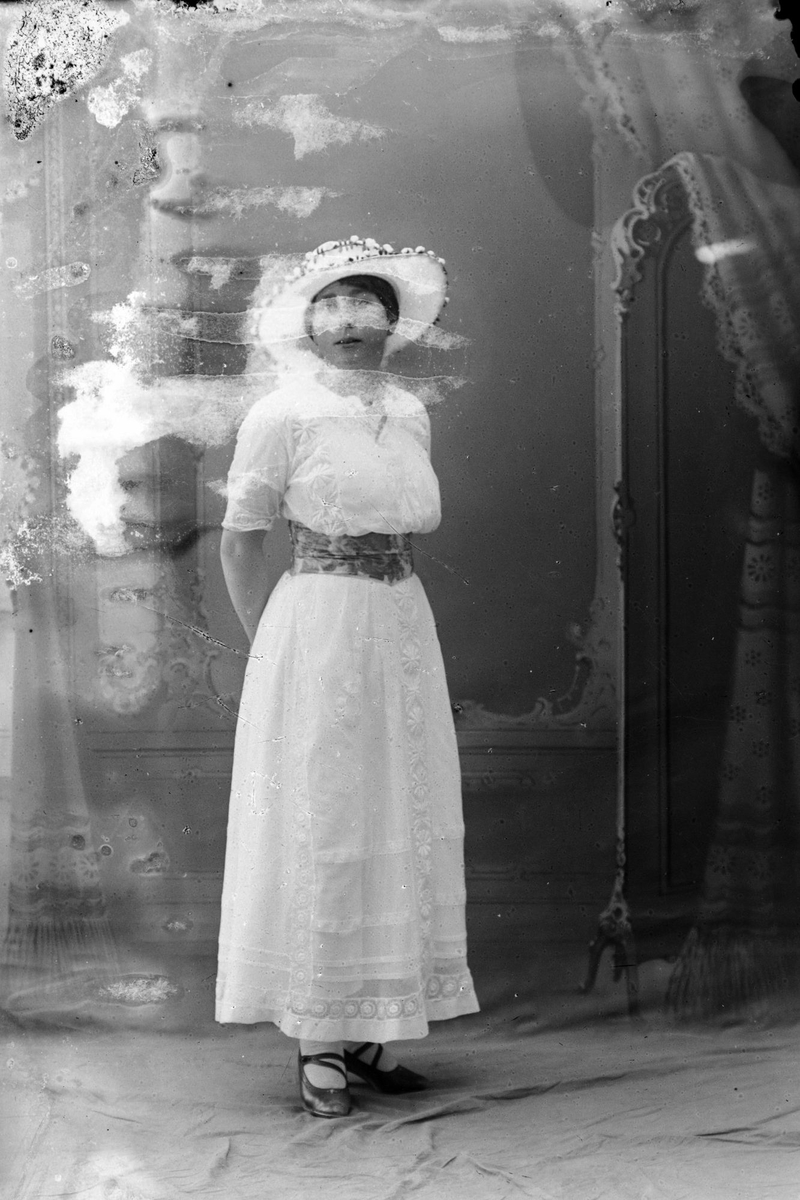 Studioportrett av en kvinne i en hvit kjole.