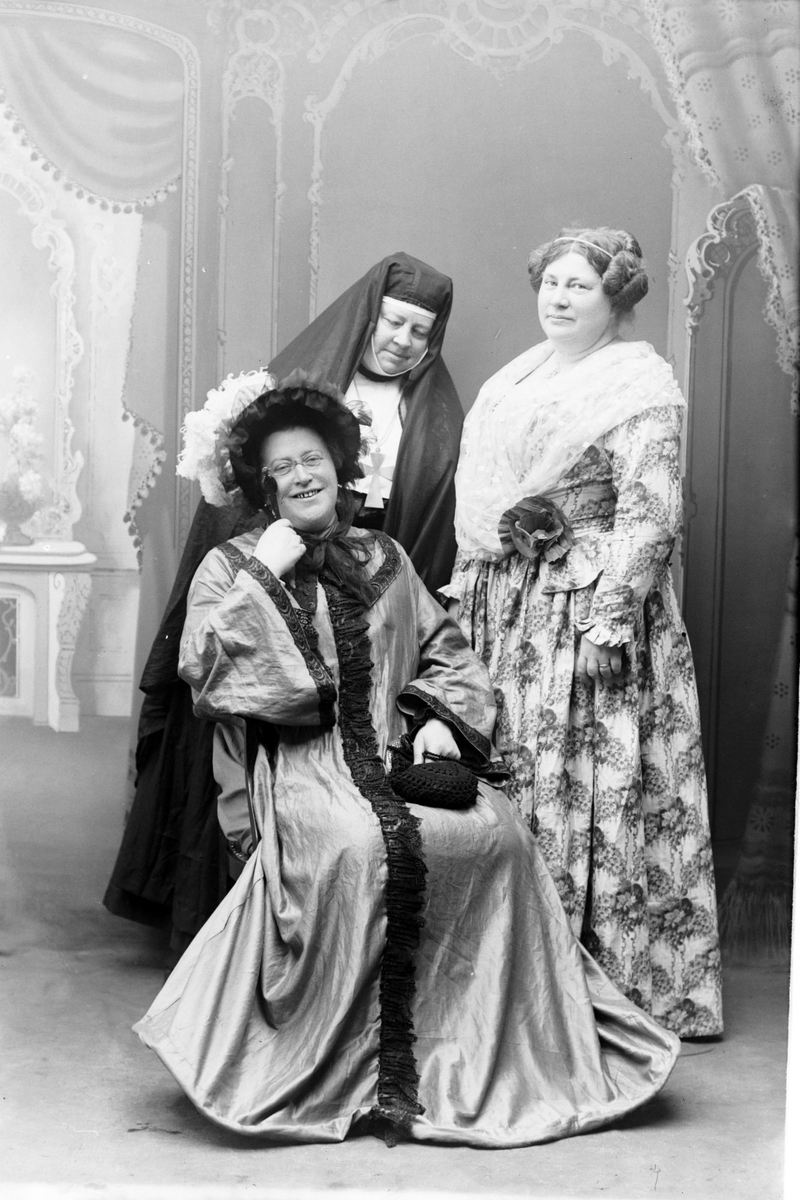 Studioportrett i helfigur av tre kvinner i kostymer.