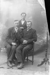 Studioportrett av to menn sittende foran én som står.