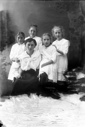 Studioportrett av en kvinne omgitt av fire unge jenter.