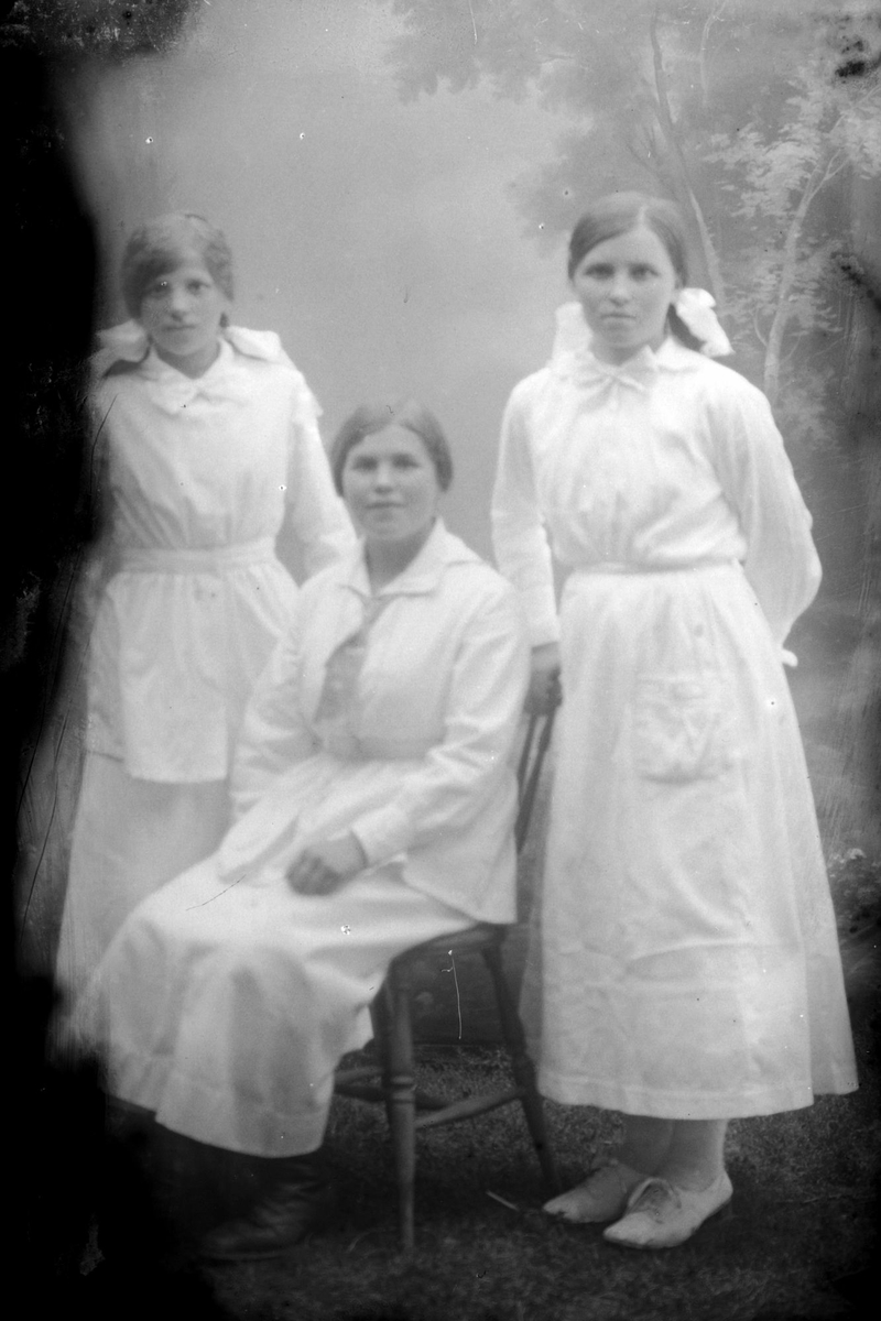 Studioportrett av tre kvinner i lyse kjoler.