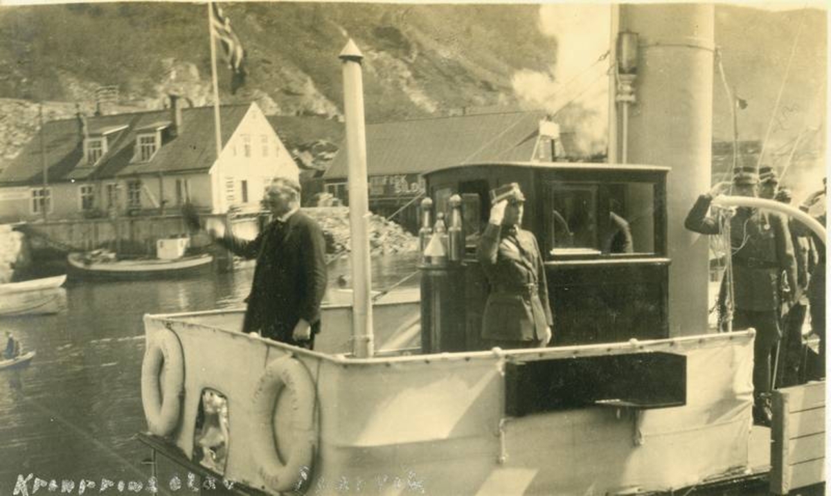 Offiserer ombord på broen på dampbåt, Krinprins Olav i løytnantsuniform hilser.
Brygger i bakgrunnen i Kleiva
Kronprins Olav kom med "Thomas Angell" fra Harstad 3. juni 1925, og reiste med "Barøy" til Bjerkvik dagen etter.
 Påskrift på bildet: "Kronprinsparet---"?