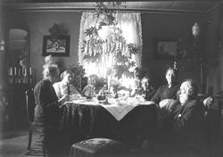 Seks personer samlet til selskap rundt et bord i stuen. Aago