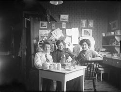 Tre damer sitter inne ved et  bord. Magdalene, Magda (fra Di