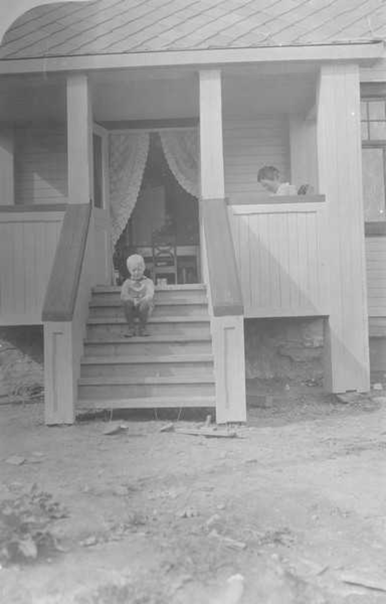 Dame sitter i vindfanget på en bolig mens en gutt sitter i trappen.