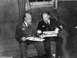 Gruppebilde. 2 personer, menn i militæruniform sitter i en s