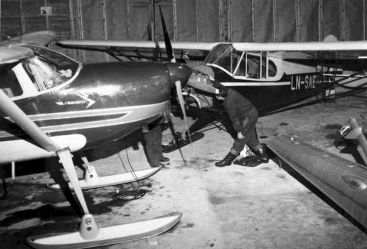 To fly og noe utstyr inne i en hangar. En person ved flyene. Flyet bak er LN-SAE