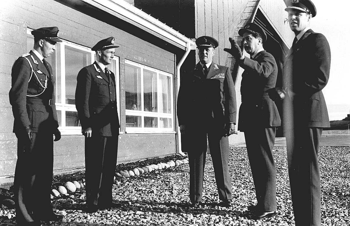 En Kronprins og militære offiserer forran en bygning og en hangar.