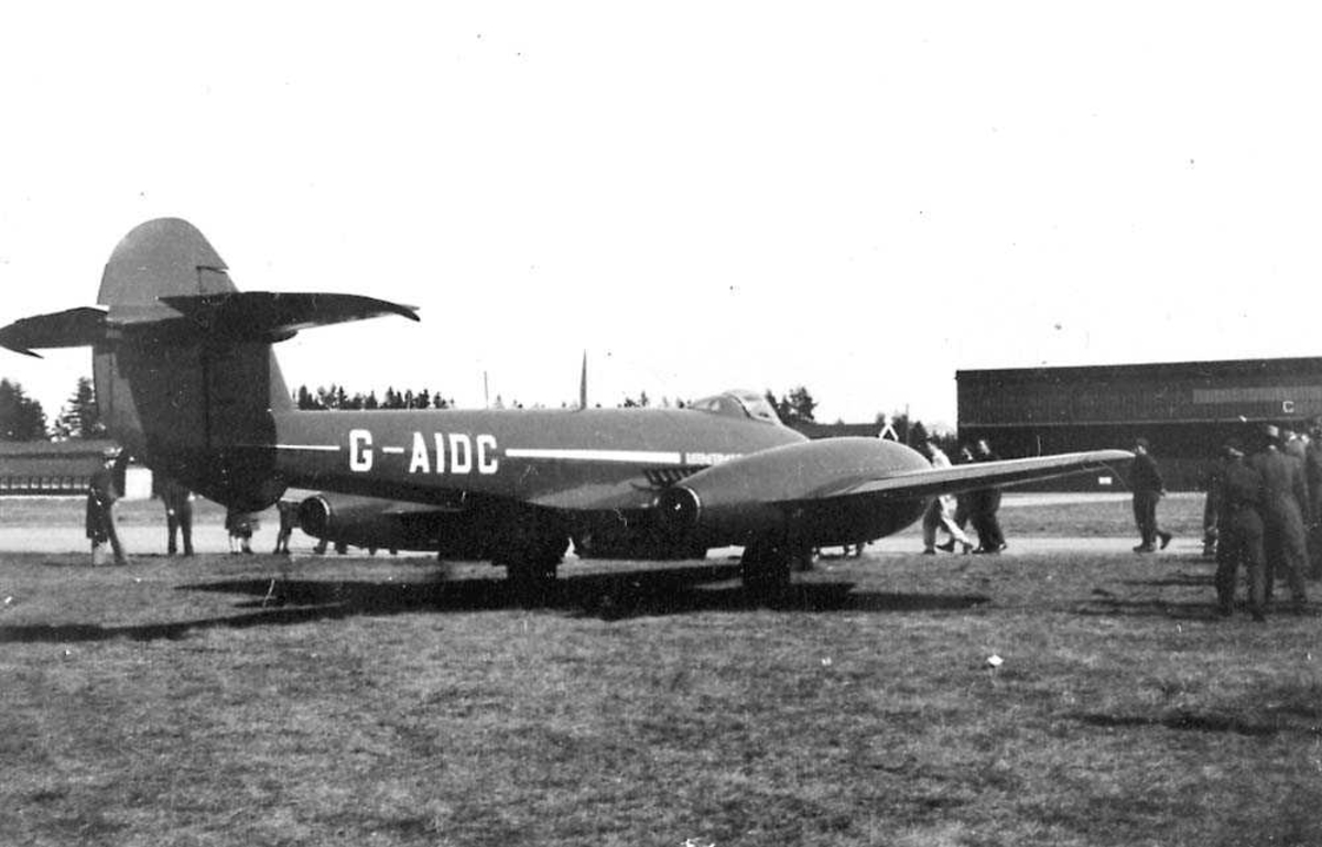 Ett fly på bakken, Gloster Meteor Mk IV. Flere personer rundt flyet. Bygning i bakgrunnen.