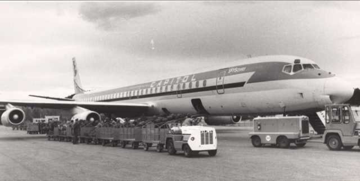 Ett fly på bakken. Douglas DC-8. Flere personer ved flyet.