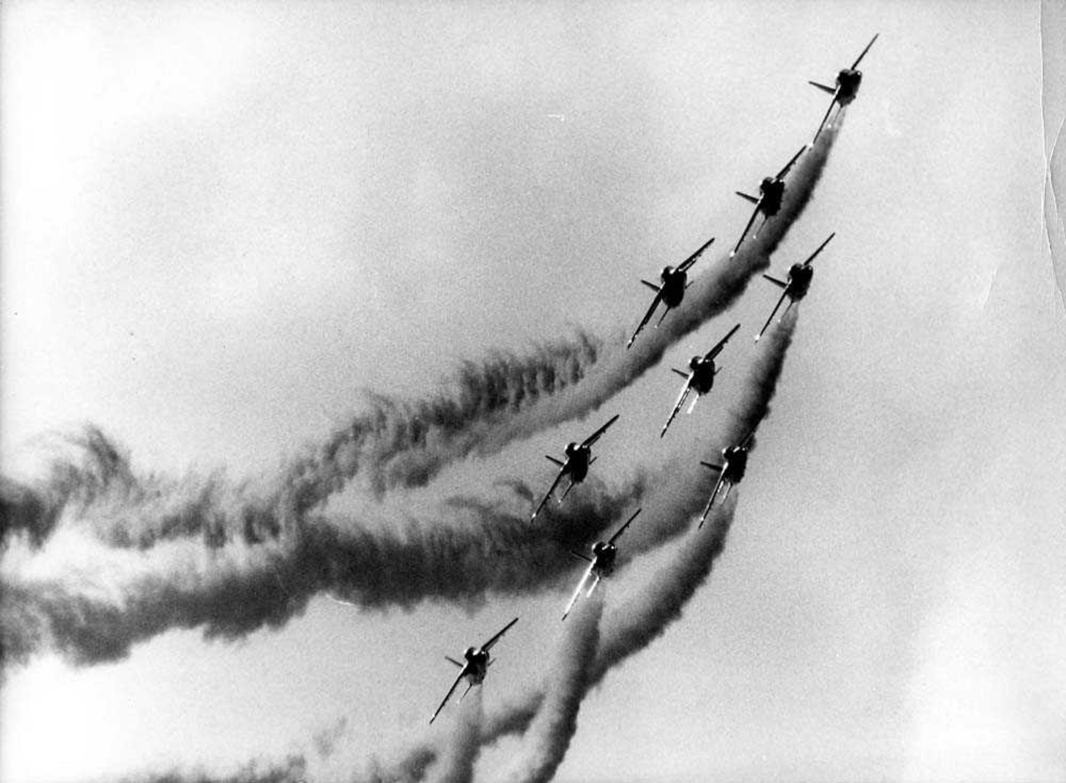 Luftfoto. Ni fly i formasjon i luften, Folland Fo.141 Gnat fra Red Arrows. Fem av flyene sender ut røyk etter seg.