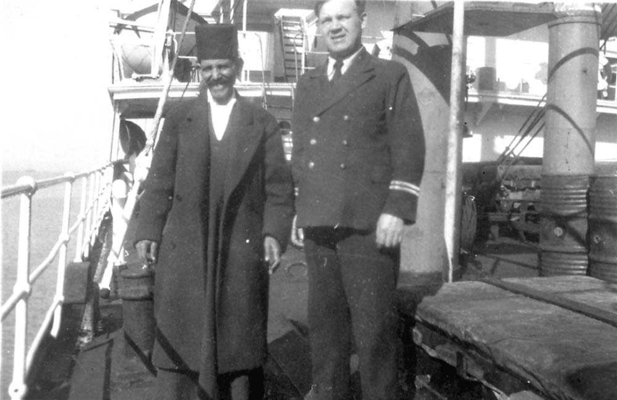 Portrett. To personer som står på dekket til en båt, en i uniform.