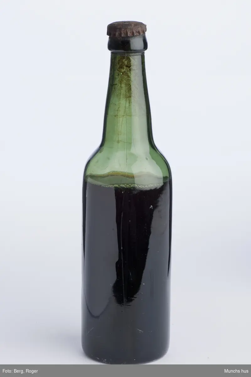Ølflaske i grønt glass. Med kork. med innhold, antakelig øl.
Tekst på kork: Frydenlund.
