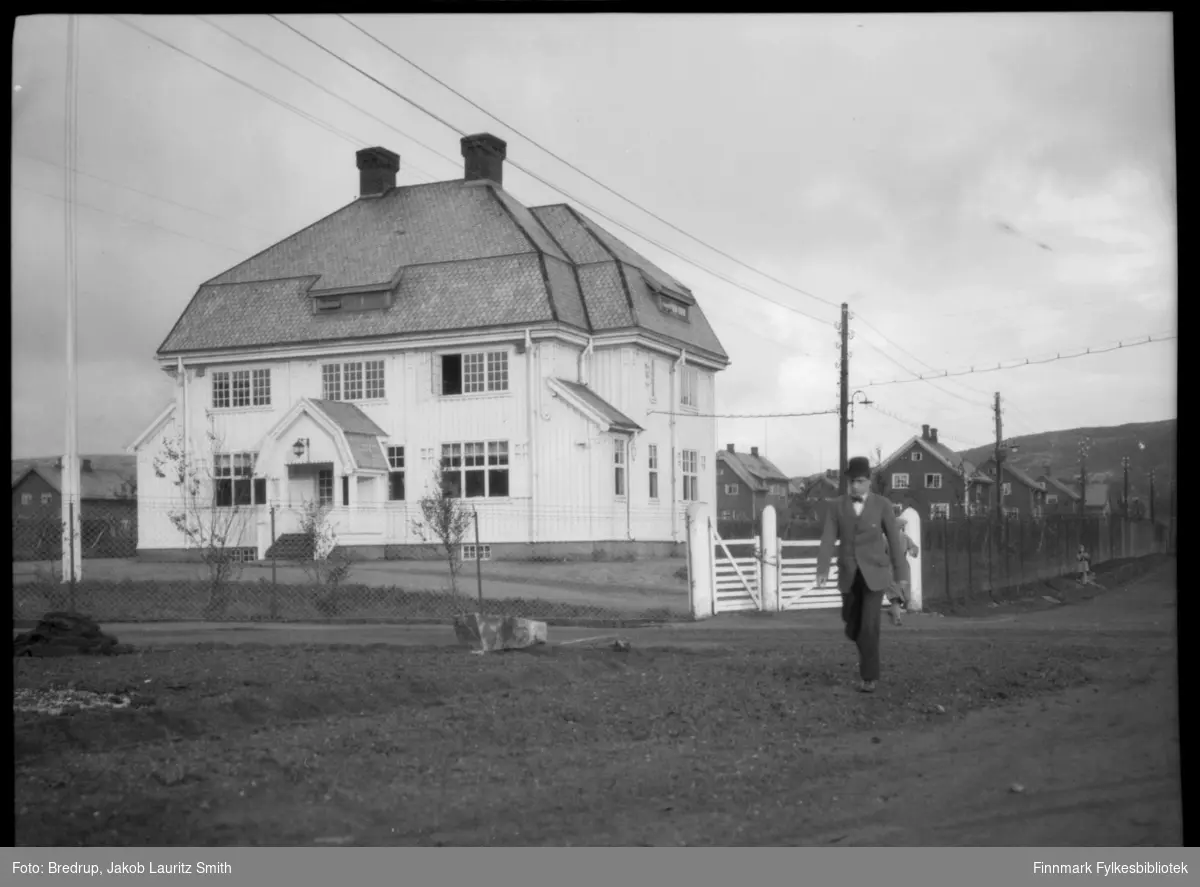 En mann med hatt passerer A/S Sydvarangers administrasjonsbygg i Solheimsveien i Kirkenes.