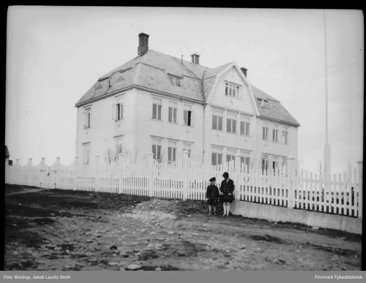 Statens kysthospital i Hvistendahlsgate i Vadsø.  Hvitt stakittgjerde rundt bygninga, to jenter står foran gjerdet.