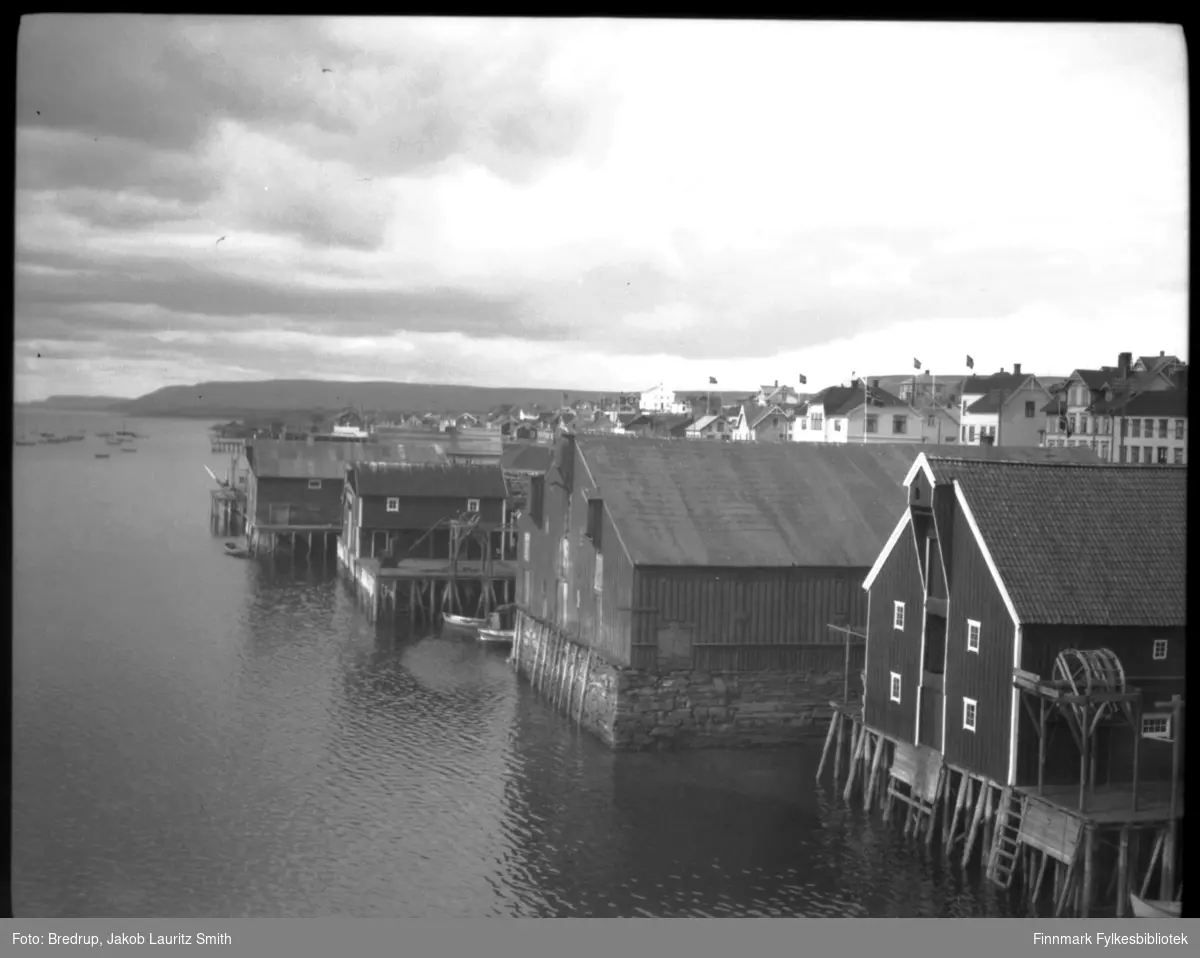 Vadsø havn fotografert mot vest.  Man ser pakkhus, kaier, havna med båter, bebyggelsen i Havnegata.  Bildet er tatt 17. mai 1933, det flagges i byen.