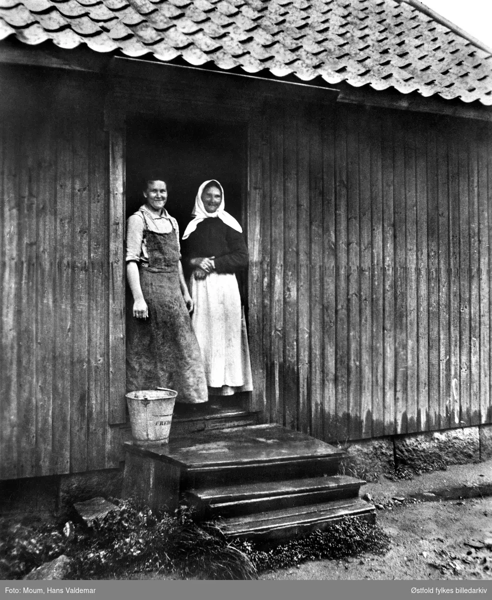 Mor og datter i bryggerhusdøra i Hans Nielsen Haugesvei (Hauge østre), Rolvsøy ved Fredrikstad -  vaskedag, ca. 1915. 
Helga Jakobsen f. Moum med langt strieforkle, og hennes mor Ellen Moum.