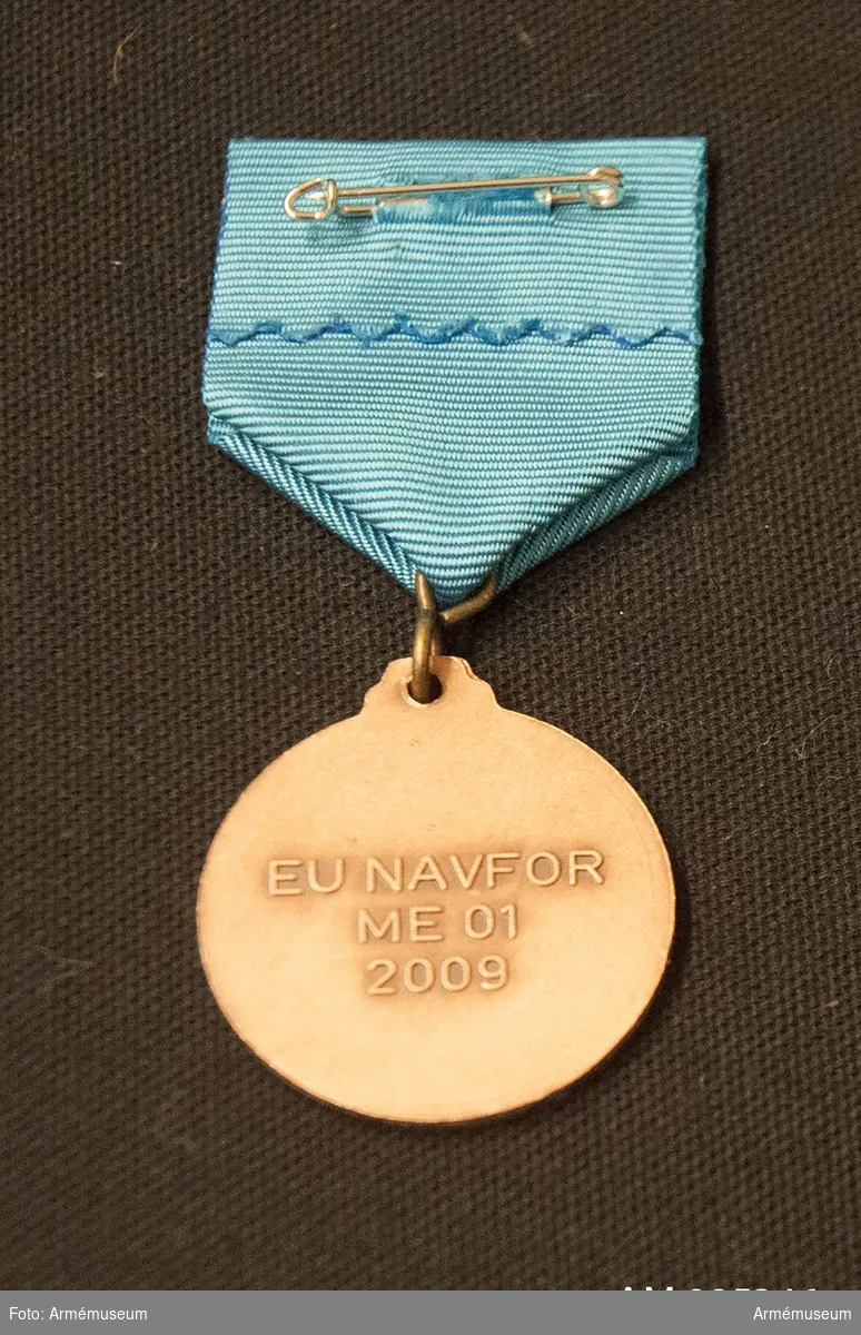 Medalj och släpspänne med blått band i blå ask klädd med mörkblå sammet och vit siden.