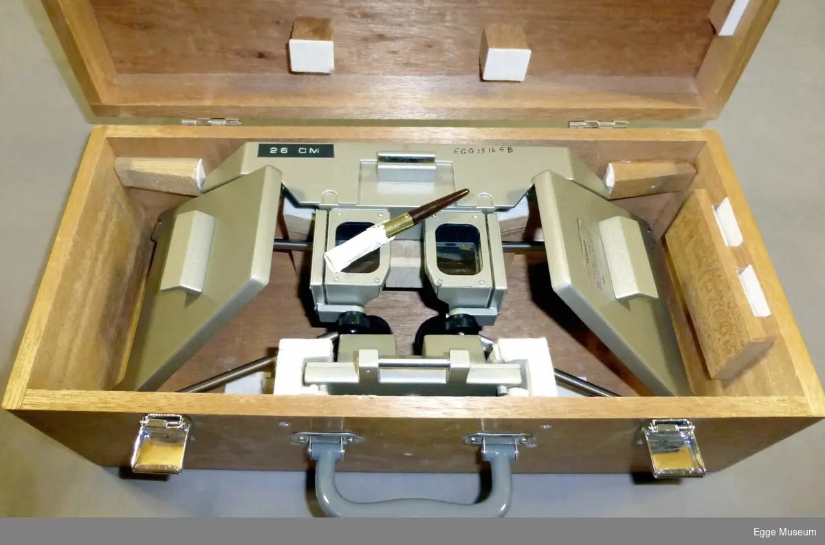 EGG.15165a. Speilstereoskop i brennlakkert metall. Stereoskopet er plassert over et stereopar av flyfoto(kontaktkopier). I stereoparet er litt over halve arealet synlig på begge bildene. Bildene er fotografert fra to forskjellige punkt med fly. Forskjellige opptakspunkt over samme område gjør at det man ser med høyre øye på høyre bilde og v. øye på v. bilde, gir et "stereoskopisk" (tredimensjonalt) bilde med høyde og relieff. Okularet over bildene forstørrer og gjør det mye lettere å lese detaljer. Stereoskopet ble brukt når det skulle gjøres terrenganalyse, så som skoginndeling, høydemåling av trær, stigning osv. (se høydemåler for stereofoto). Dette prinsippet er grunnlaget for konstruksjon av høydekurver på topografiske kart. Kunnskap om flyfoto var viktig for fagfolk i skogbruket.  På finerplata under stereoskopet er det montert et stereopar. Gjebstanden består av tre deler. Merket Topocon Corporation, Made in Japan og Gundersen og Løken, Oslo.

EGG.15165b samme som a, men med lakkert transportkasse i tre og rensebørste. Klipslås og plasthåndtak på transportkasse. Merket Topocon Tokyo Kogaku Kikai Co., Ltd, Made in Japan.  
EGG.15165c samme som b, men merket Topocon Corporation Made in Japan, M705
blastbeslag foran glass og med nøkkel til lås.

Landmåling var en svært viktig del av skogbruksutdanninga før 2. verdenskrig. Den ble mindre viktig etter krigen, da det etterhvert kom mer moderne målemetoder. Brukt i undervisninga ved Skogskolen i Steinkjer.