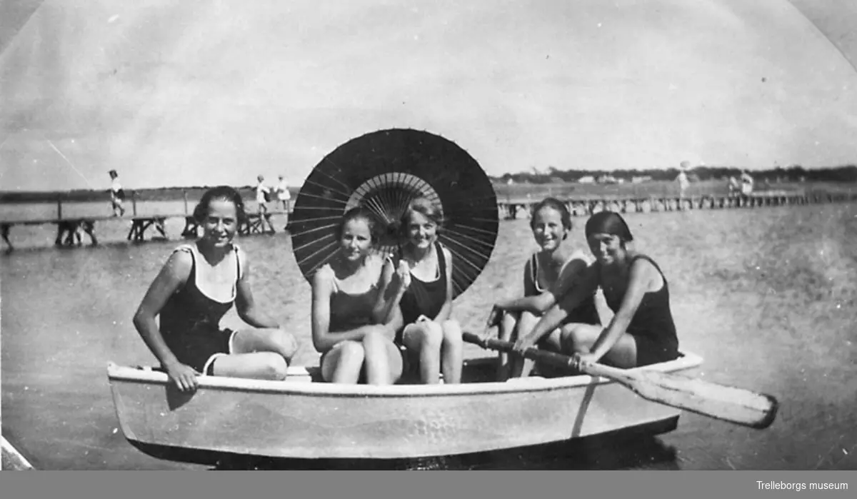 Fem kvinnor i baddräkter i en eka vid stranden.