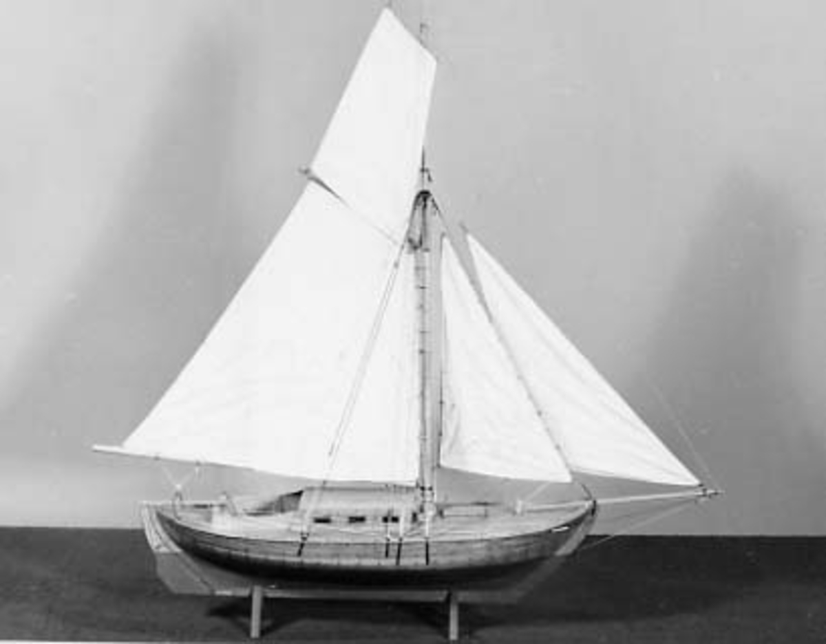 Modell av Falkenholms segelbåt  "FALKEN 1834". Däckad lustjakt av kostertyp, helt klinkbyggd och riggad med segel. Ruff och sittbrunn byggd av ek. Däck av furu med svarta nåt.  Fernissad med röd botten. Rigg med taljerep, hög mast, klyvarbom och fyra segel. Skrovets l.ö.a.:  48 cm bredd 17 cm.