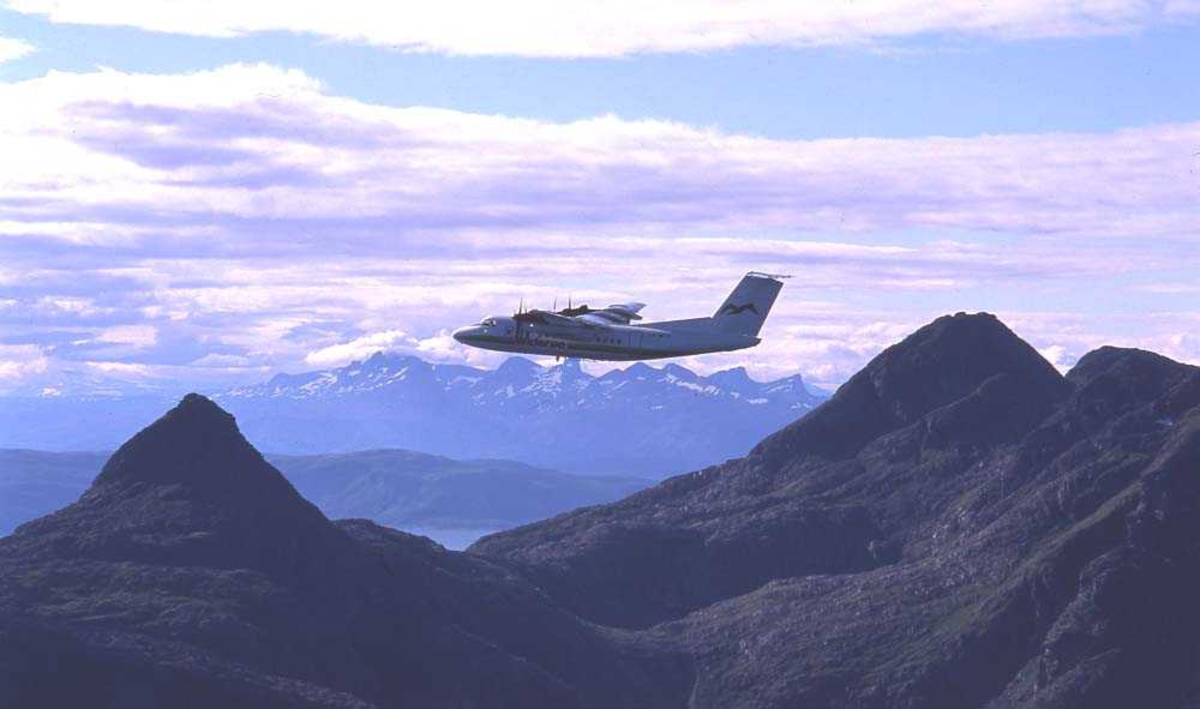Luftfoto. Ett fly, LN-WFK, DHC-7-102 / Dash7 fra Widerøe passerer over Landegode utenfor Bodø. I bakgrunnen ses fjellkjeden Børvasstindane.