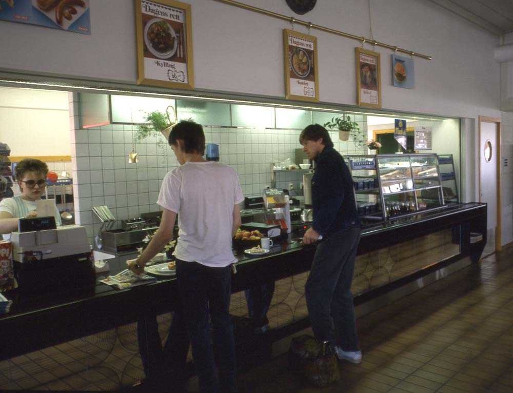Lufthavn/Flyplass. Stokmarknes/Skagen. Interiørbilde fra flyterminalens kafeteria. To personer kjøper mat og kaffe før avreisen.