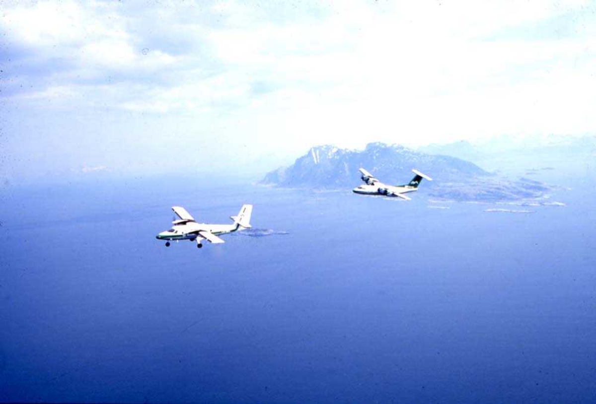 Luftfoto. To fly, LN-WFG, DHC-7-102 Dash7 og LN-BNM, DHC-6-300 Twin Otter fra Widerøe passerer sørenden av Landegode som ses i bakgrunnen.