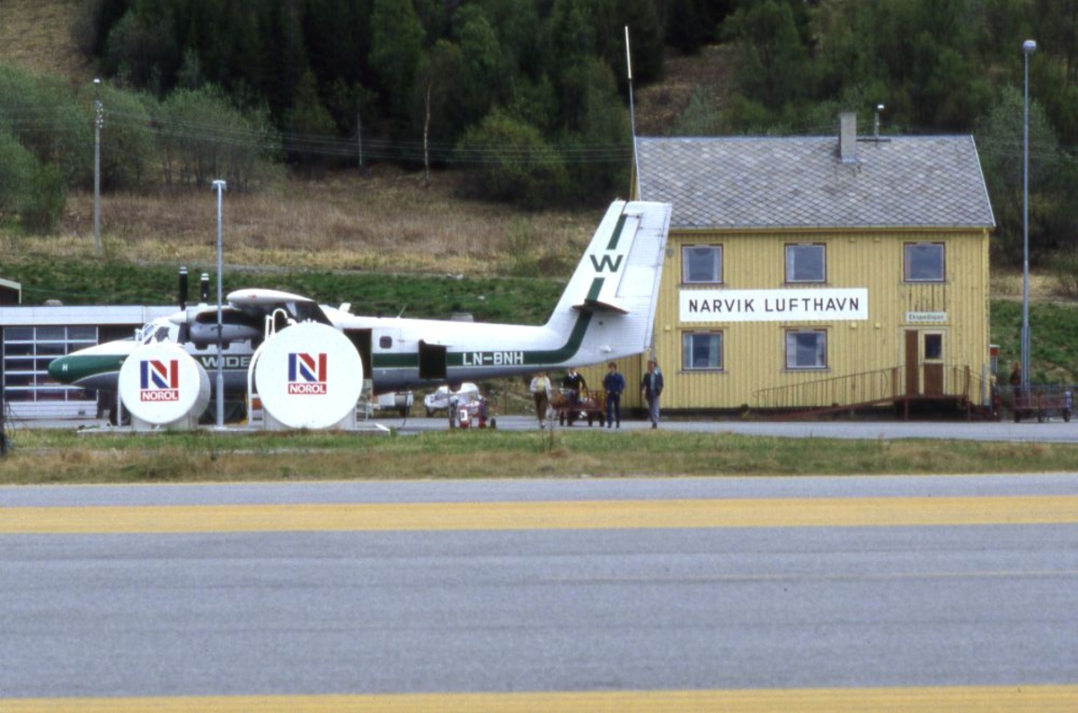 Lufthavn (flyplass). Et fly, LN-BNH, DHC-6-300 Twin Otter fra Widerøe, parkert foran Flyekspedisjonen. Flere personer ved flyet. I forgrunnen tankanlegget.