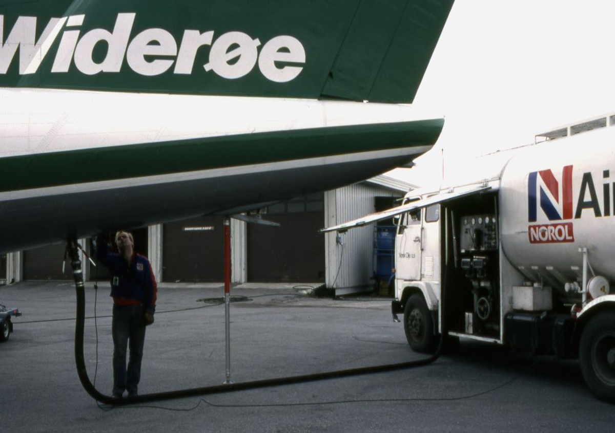 Lufthavn (flyplass). En person iferd med å fylle tankene med drivstoff (fuel) fra en tankbil, på et fly, DHC-7-102 Dash 7 fra Widerøe.