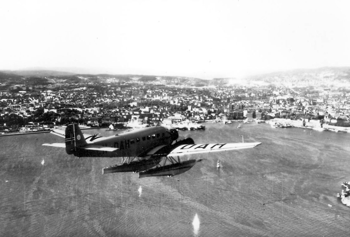 Luftfoto, ett fly i luften, Junkers Ju 52/3mg2e, LN-DAH, "Falken". Hav og tettsted/by sees nedenfor.