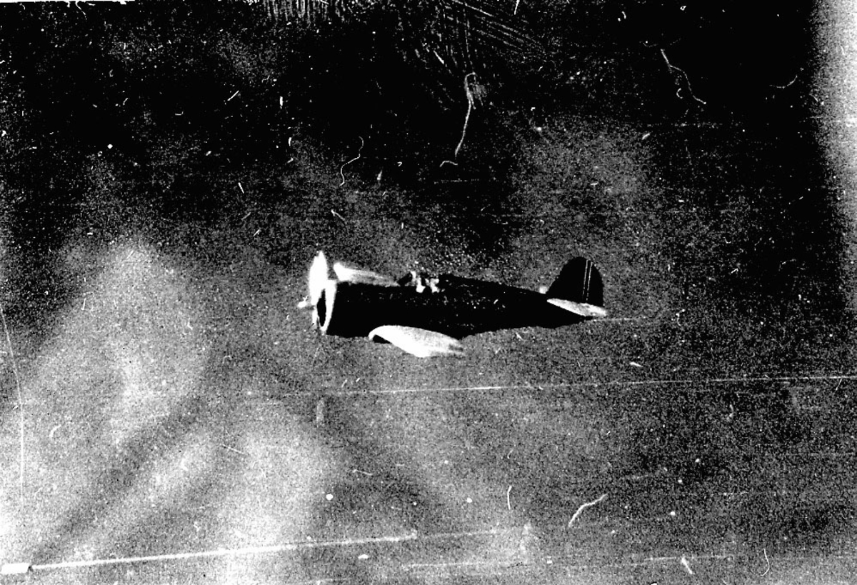 Luftfoto, et fly i lufta, sett fra siden, litt ovenfra. Landskap under. Piloten sees i coskpiten.