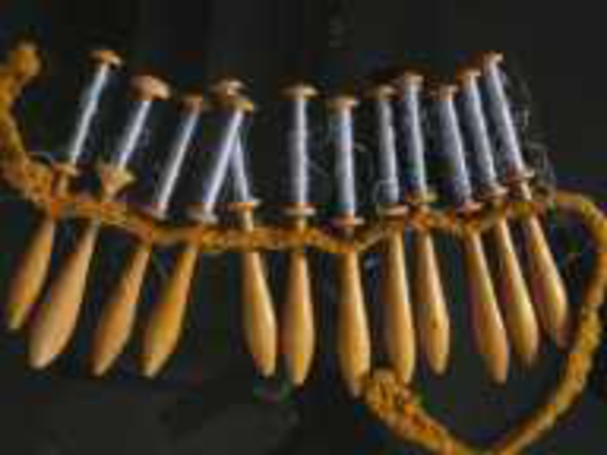 Små trådsneller m. håndtak. Alle er påviklet tråd i gråblå farge og er festet i en hullet snor til bruk på knipleputa. Er trolig brukt til et kniplearbeid og er klippet av og lagret med trådrestene i behold.
