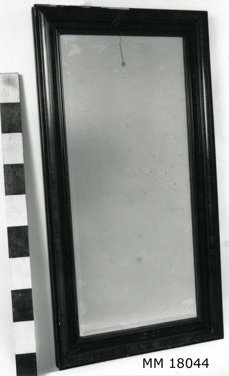 Rektangulär spegel med slipat glas, profilerad ram, imitationsmålad i trä, B = 100 mm. Baksida klädd med kartong. Skrivet för hand: " Örlogshemmet ". Öglor och snöre för upphängning.