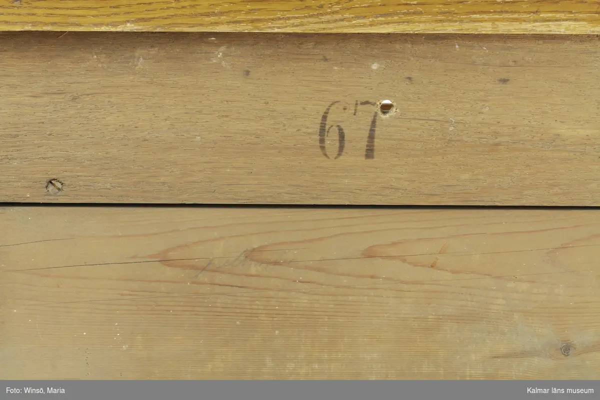 KLM 45337:1-2. Riksdagsstol. Består av en pulpet och en taburett. Pulpet (:1) av lackat trä med detaljer av metall. På pulpetens ena sida ett sluttande skrivbord med lock och lås. I högra hörnet hål och lock för bläckbehållare. Inuti bänken sekundärt skrivet med blyerts: C.A.A. * 18 9/8 46 (?). Nedan bänken ett tvärgående fotstöd. På pulpetens andra sida ett fastskruvat ryggstöd samt två armstöd. Dessa är stoppade med tagel och klädda med ett vinrött bomullstyg. På ena armstödet saknas tyget och ett vitt undertyg är synligt. Armstödens främre del är klädda i brunt läder. Ryggstödet kan lossas med en skruv och bakom, på pulpeten, siffrorna 67 i svart färg. Med blyerts även skrivet: Pettersson. På ryggstödets baksida, på sargen, möbelsnickarens stämpel, ett N inom en taggig oval ring. Även 166 i svart färg. Hela möbeln har svarvade raka, rektangulära ben och tvärgående fötter. Överstycke med svarvade knoppar och utsparade detaljer. På överstyckets mitt en mässingsplåt med instansade siffror: 77. Till pulpeten hör en taburett (:2) som, när det placeras intill ryggstödet, blir en stol. Taburetten är av lackat trä med svarvade kryssben och mittslå. Under två av benen små trähjul. Stoppad löstagbar sits klädd med likadant vinrött tyg som på pulpetens ryggstöd. Sitsen går att lossa och på dess undersida är möbelsnickarens signatur stämplad i träet: F. RAMBACH. Även 67 i svart färg. På sargen är det också siffror och bokstäver skrivet med blyerts: 97, IK eller IJG. På taburettens sarg spår efter stämplar: 54, 52.