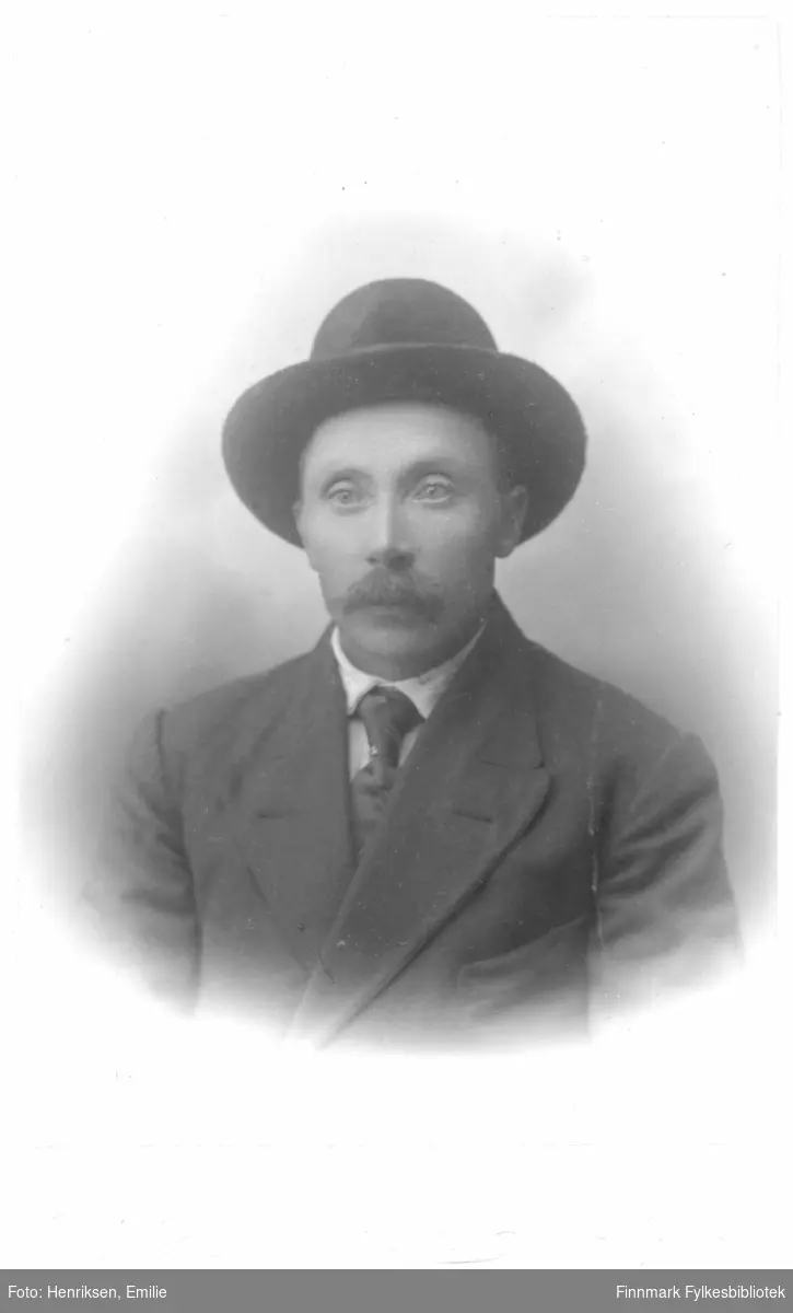 Portrett av en mann med bart og hatt, ikke identifisert. Han er kledd i dobbeltspent dress med slips og har en hatt med brem på hodet.