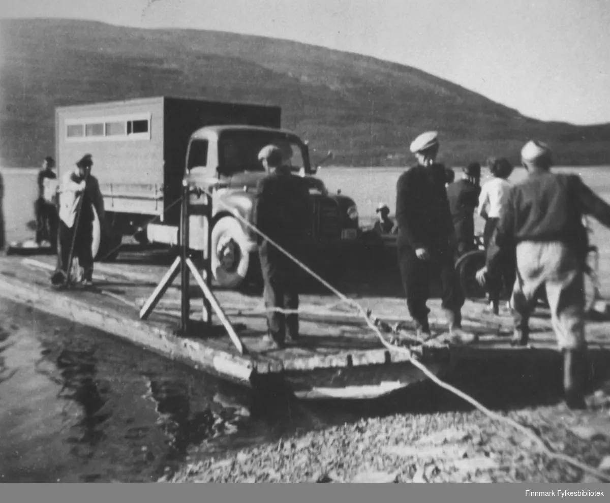 På ferge over Tanaelva ved Langnes, 1954. Hjemtur fra Kongsfjordfjellet. På bildet ser man ferga med en lastebil (Austin Loadstar) og noen mennesker ombord.