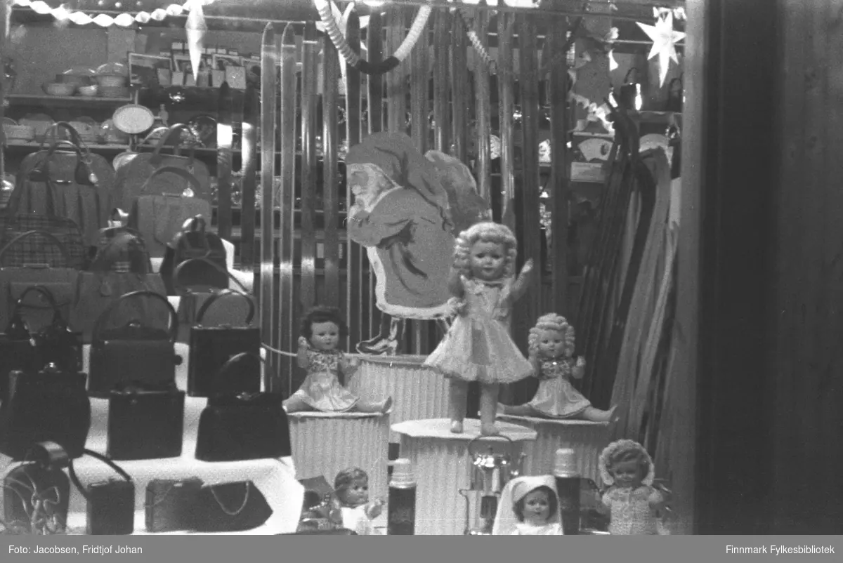 Juleutstilling i butikken til Trygve Nissen etter andre verdenskrig. Små søyler med dukker og nisser står til høyre på bildet mens håndvesker står til venstre. Bak denne utstillingen står en del langrenns-ski. Et par stjerner ses øverst på bildet og en del andre saker står på hyllene i bakgrunnen.