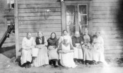 Fotografi av åtte ukjente eldre kvinner som sitter på en ben