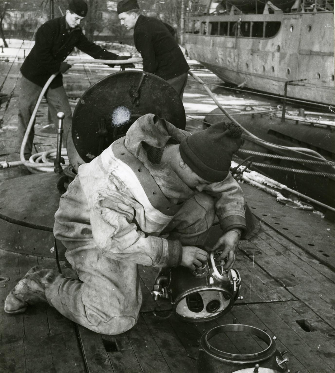 Dykarbete på ubåten Sjöormen 1949.
Tungdykare kollar hjälmen på däck. Fartyget förtöjt vid Skeppsholmen.