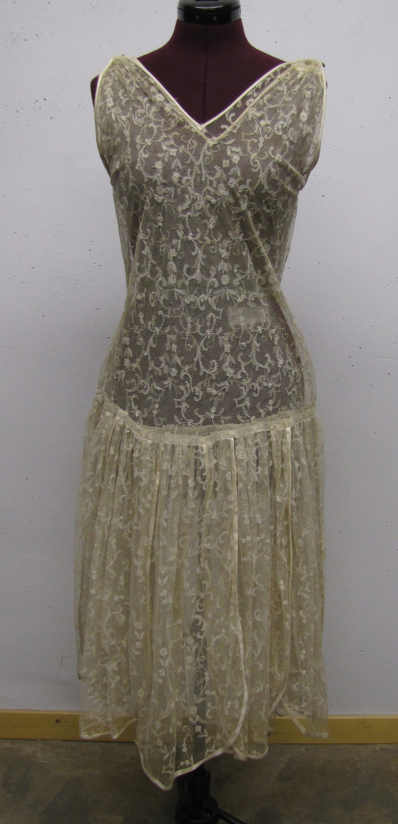 Ärmlös klänning, v-ringad fram och bak. Kjolen består av flikar, kantade med satinband.

Klänningen är från 1920-talet.