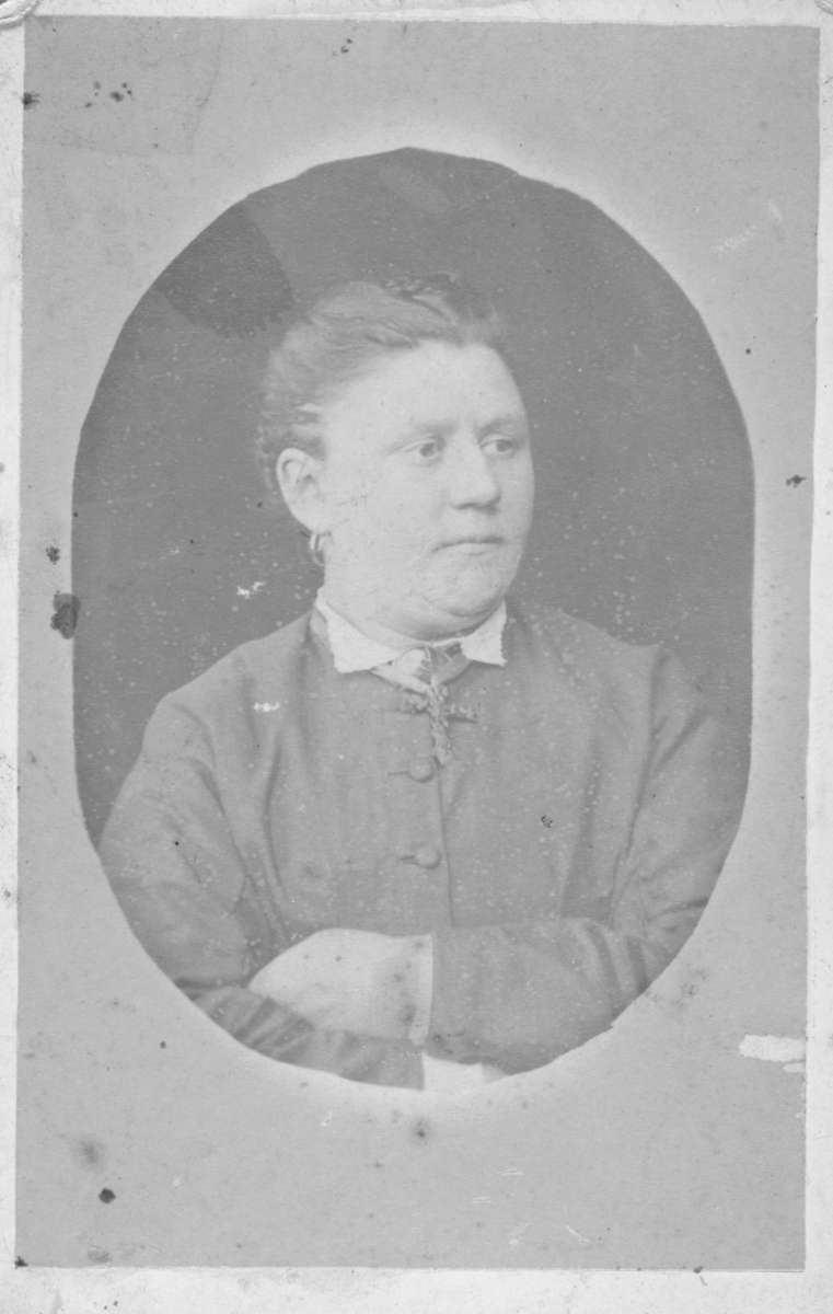 Portrett fra en eldre kvinne, (ikke identifisert). Hun er kledd i hvit bluse og draktjakke over, og hun bærer et stort kors i silkebånd rundt halsen. Bildet er tatt hos L. Schetnes' fotografiske atelier i Tromsø.