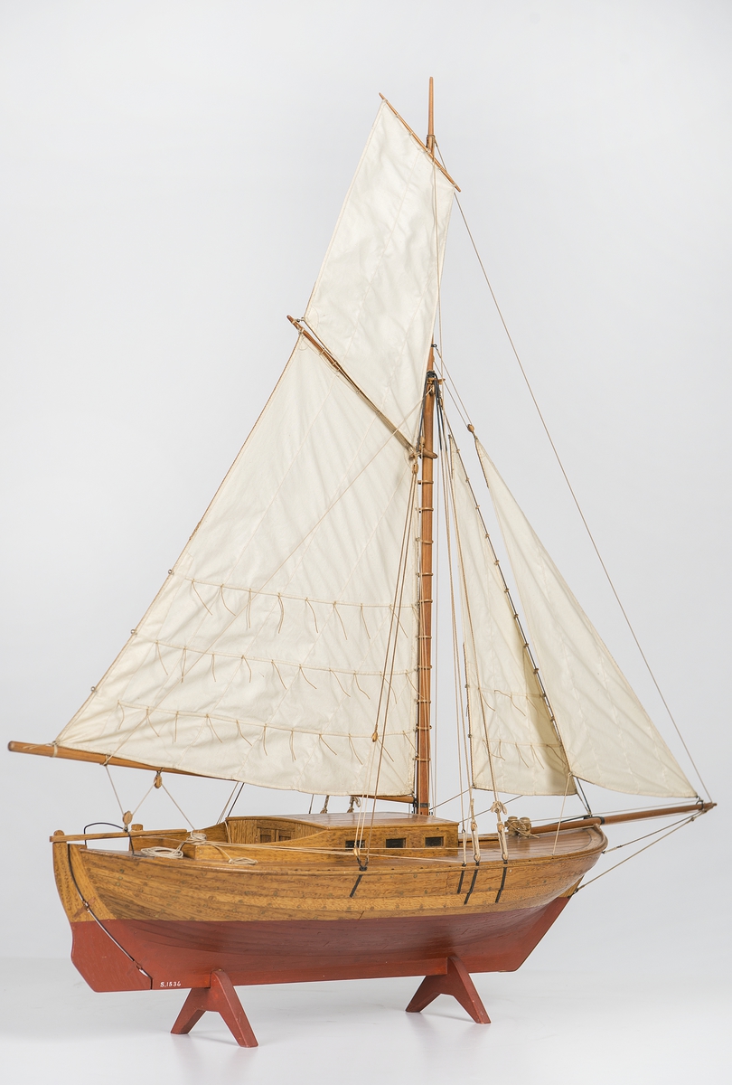 Modell av Falkenholms segelbåt  "FALKEN 1834". Däckad lustjakt av kostertyp, helt klinkbyggd och riggad med segel. Ruff och sittbrunn byggd av ek. Däck av furu med svarta nåt.  Fernissad med röd botten. Rigg med taljerep, hög mast, klyvarbom och fyra segel. Skrovets l.ö.a.:  48 cm bredd 17 cm.